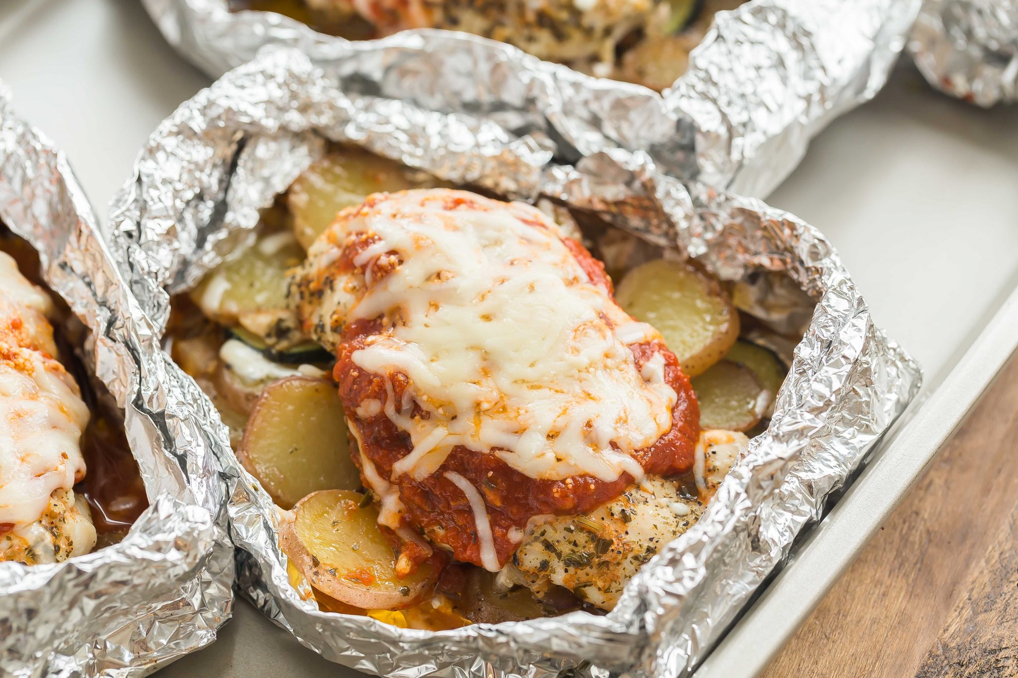 A delicious foil pack dinner with chicken breasts and little potatoes absolutely covered in cheesy goodness.