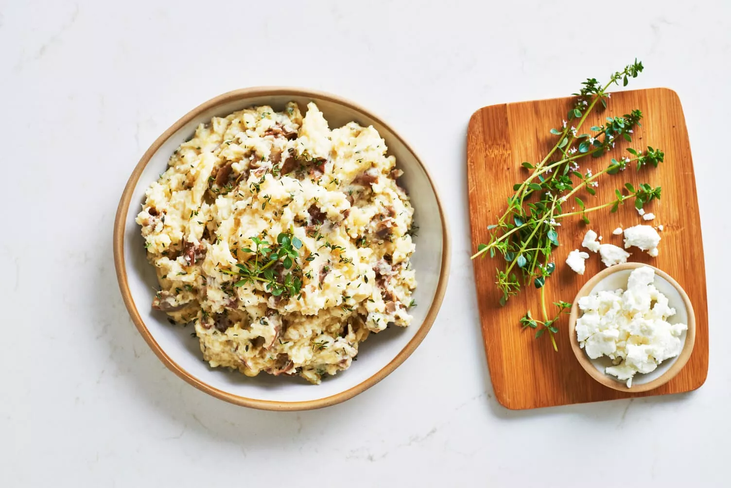 A bowl of goat cheese and thyme mashed potatoes with some sprigs of thyme nearby.